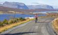Syklist på grusvei med innsjøer og fjell i bakgrunnen