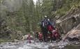 A group of persons with wetsuits and helmets walks in a river.