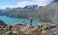 Dame på fjelltur over en fjellrygg over bregrønt vann