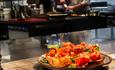 A plate with delicious food in the foreground and the restaurant kitchen with the chefs cooking in the background.