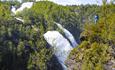 Doppelter Wasserfall in Schlucht mit grüner Vegetation. Eine Person steht an der Abbruchkante.