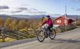 Cyclist with red jacket in mountain farming area in front of red wooden cabin