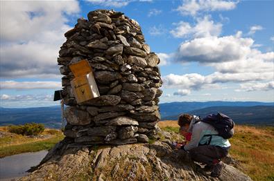 A large summit cairn on Synet. A mother and a child register their trip in the tour log book.