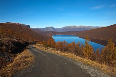 Im Anstieg der Straße über das Smådalsfjell mit Aussicht über den spiegelblanken Helin. Die Birken ind en Berghängen tragen orange Herbstfärbung. Blauer Himmel.