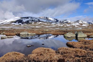 snødekte fjell speiler seg i blikkstille fjellvann