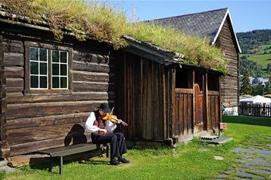 Spelemann spiller fele utenfor gammel bygning en sommerdag.