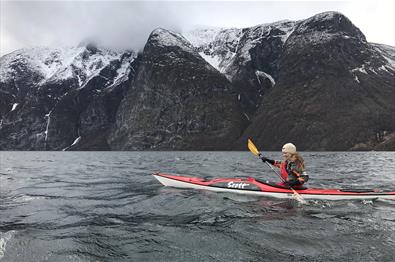 Ein Kajakpaddler auf einem Fjord mit verschneiten Bergen im Hintergrund