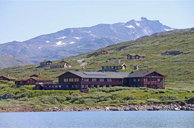 En fjellstue og et knippe hytter ved et vann i storslått høyfjellslandskap