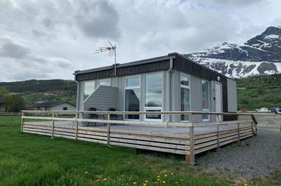 A small square wooden building with apartments, encircled by a deck. Mountains in the background.