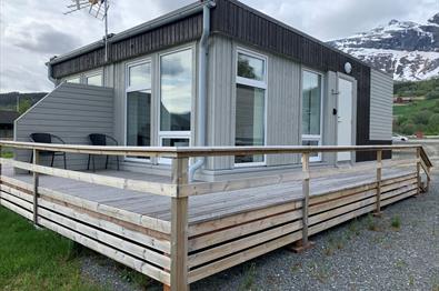 Ein kleines, viereckiges Gebäude mit Apartments, einer rundumgehenden Veranda und Bergen im Hintergrund