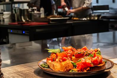 A plate with delicious food in the foreground and the restaurant kitchen with the chefs cooking in the background.