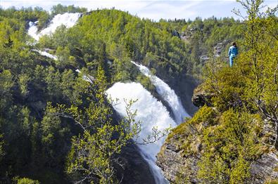 Doppelter Wasserfall in Schlucht mit grüner Vegetation. Eine Person steht an der Abbruchkante.