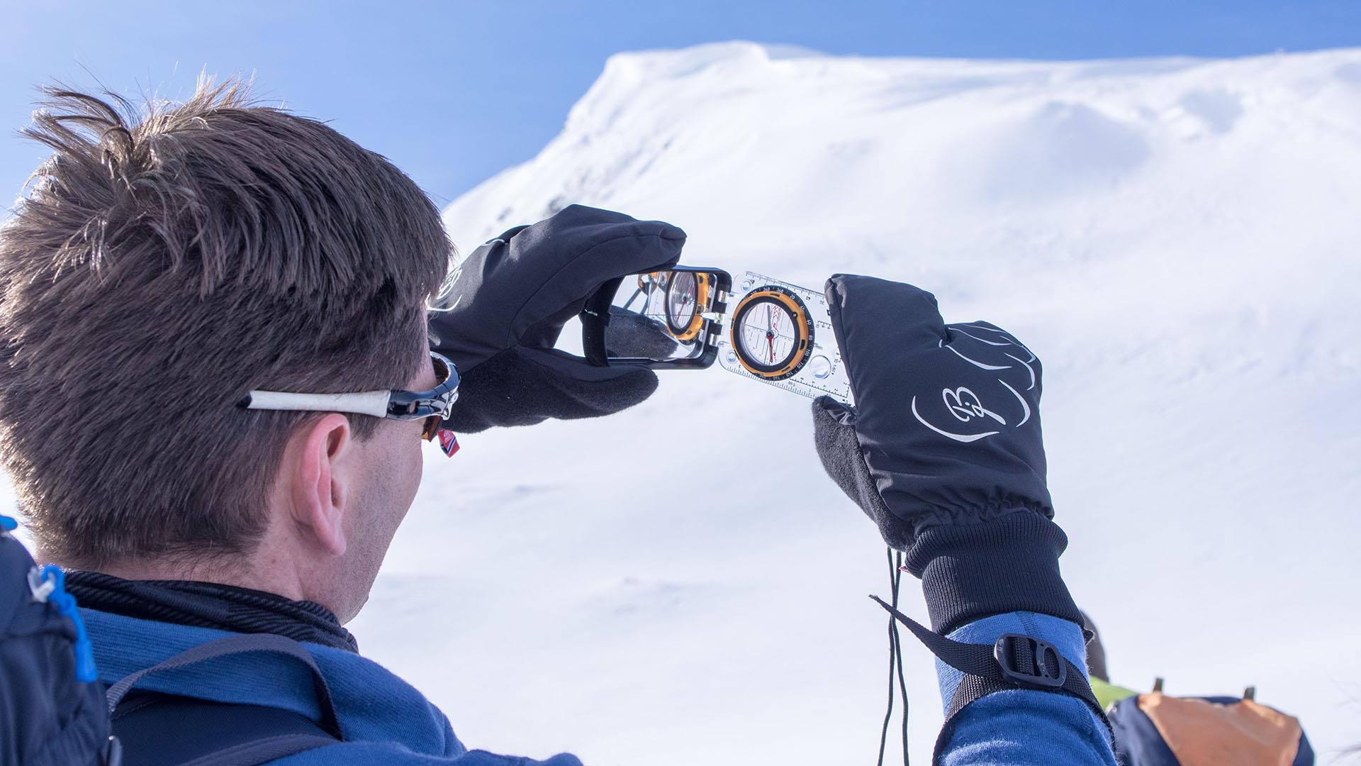 En person bruker et kompass for å bestemme helningsgraden av en fjellside i vinterfjellet.