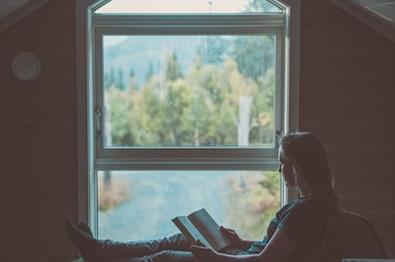 person sitter og leser bok i vinduskarmen