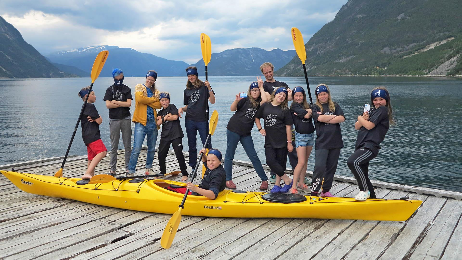 En gruppe kajakkelever og en gul kajakk på en brygge ved en fjord.