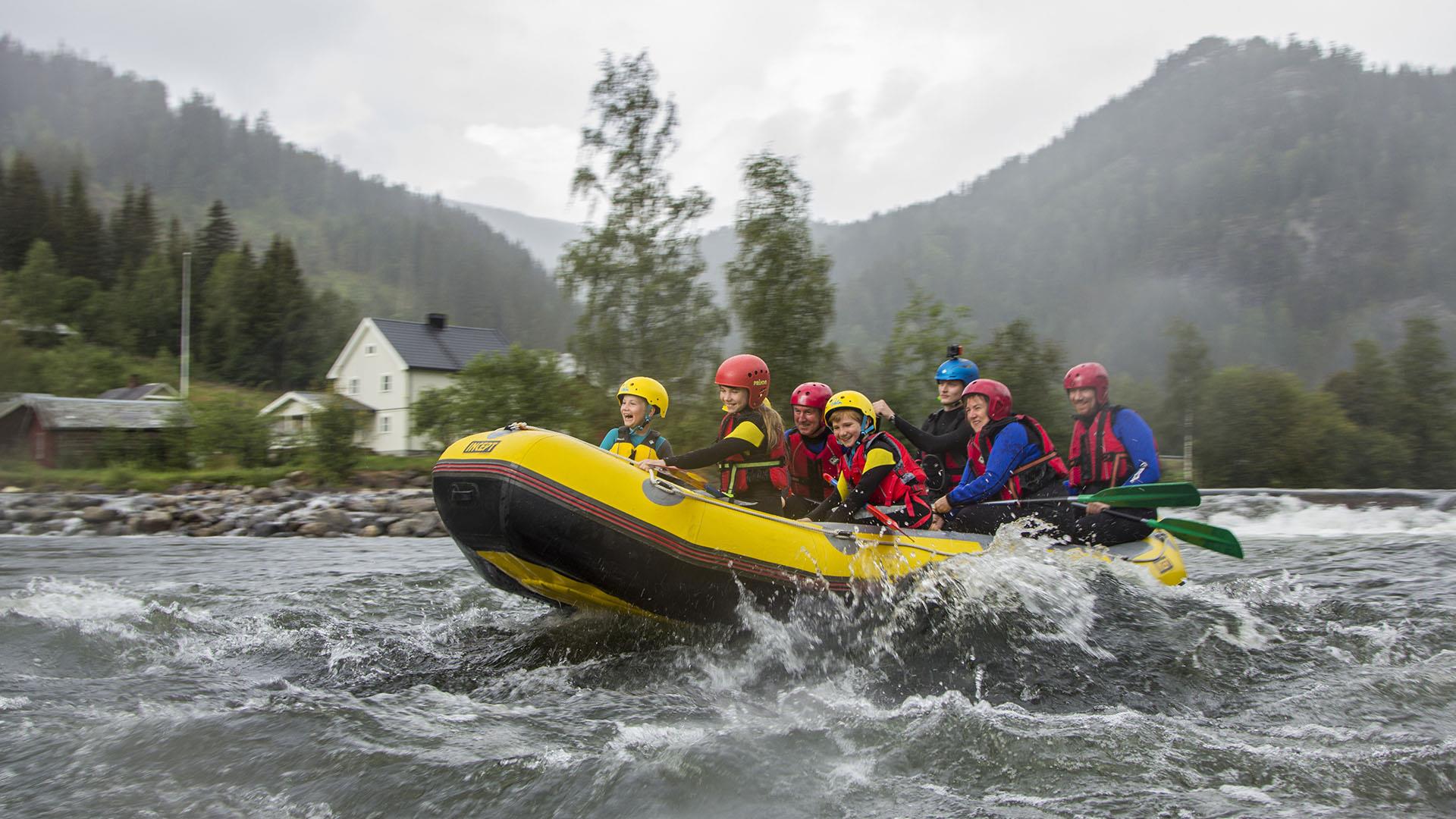 En raftingbåt med barn og guider i et stryk i en elv en gråværsdag.