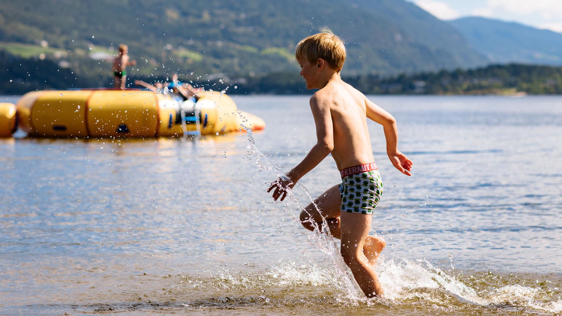 Ein Junge rennt ins Wasser. Weiter draußen im See schwimmt eine gelbe aufblasbare Spielinsel.