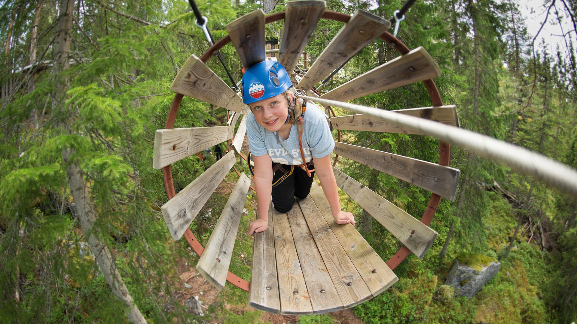 A girl crawls through a pipe made of wooden panels in a high rope course.