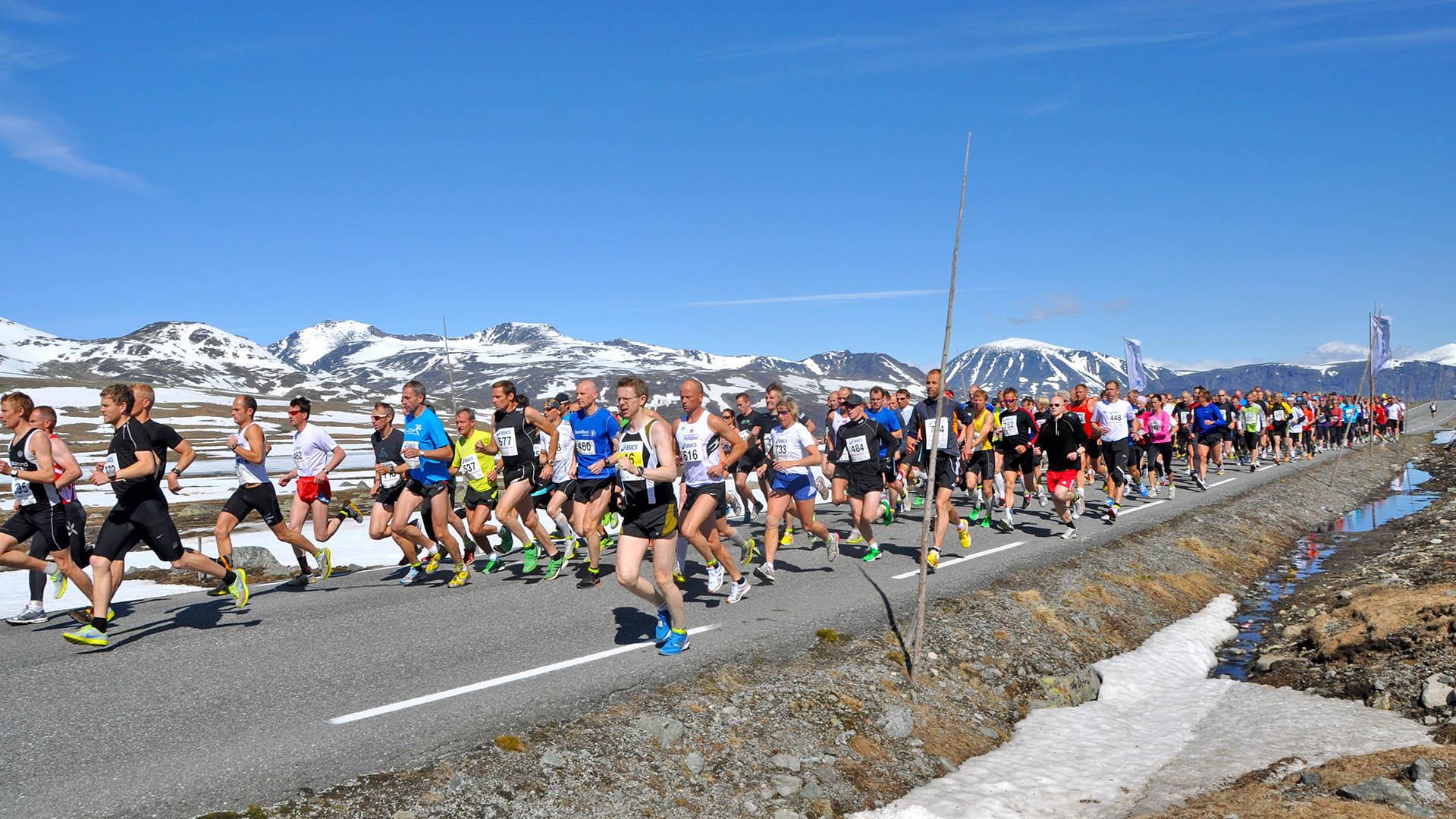 Maratonløpere på en fjellvei med totusenmetertopper bakenfor.