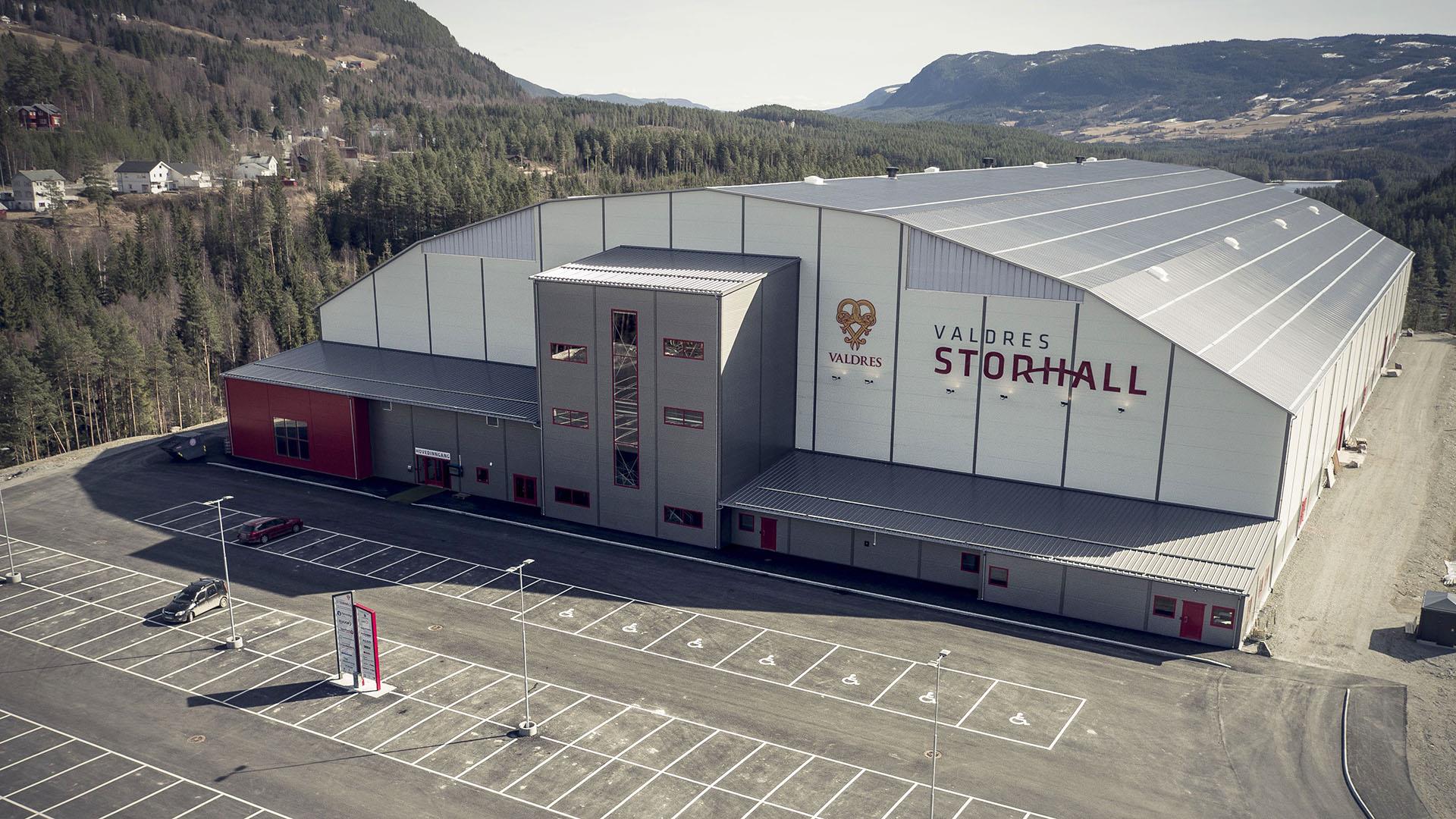 A multi-use hall for indoor activities with tha parking lot, seen from outside. The image is taken from low hight with a drone.