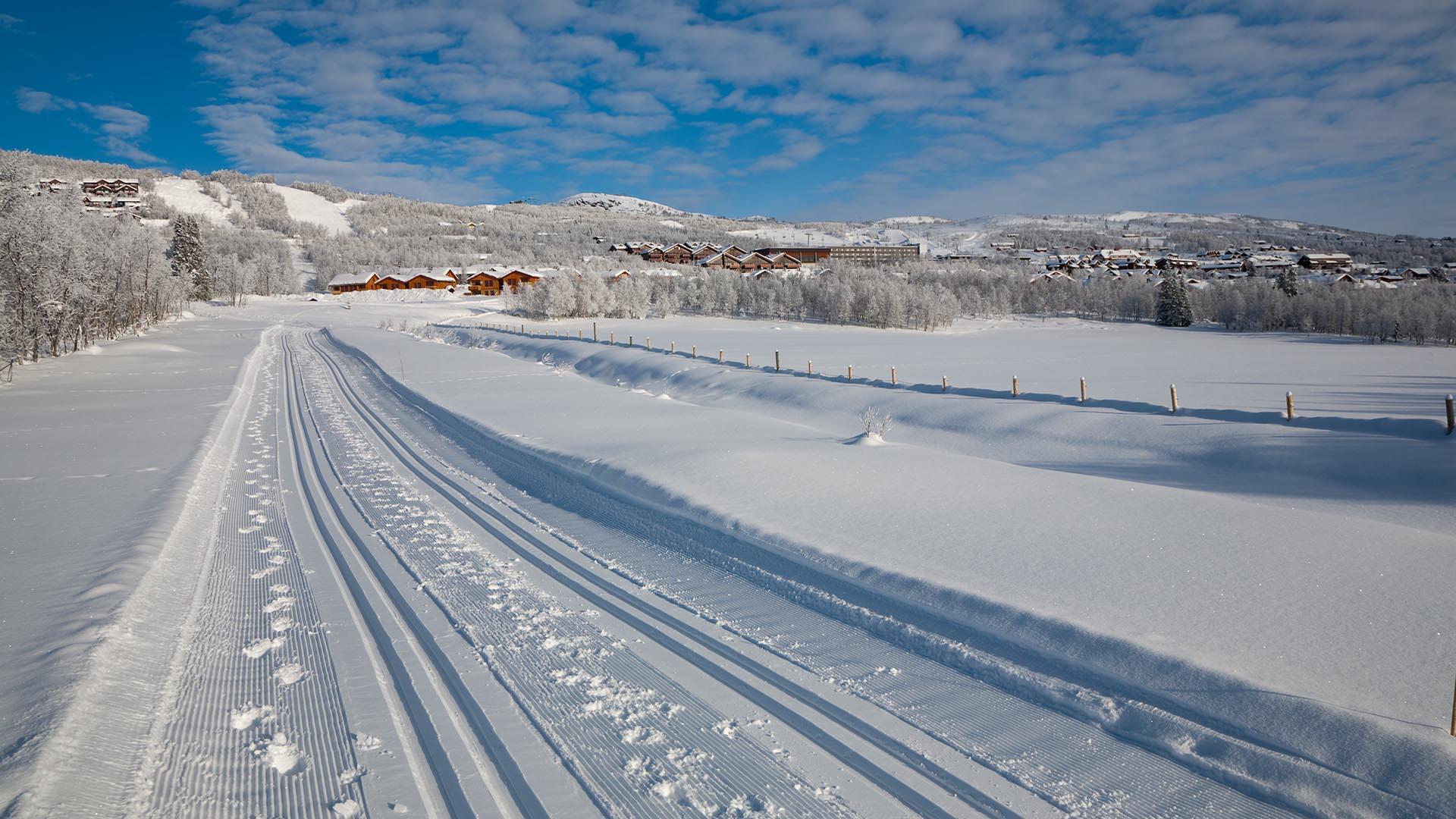 Freshly groomed cross-country skiing track over a flat area below mountain village.