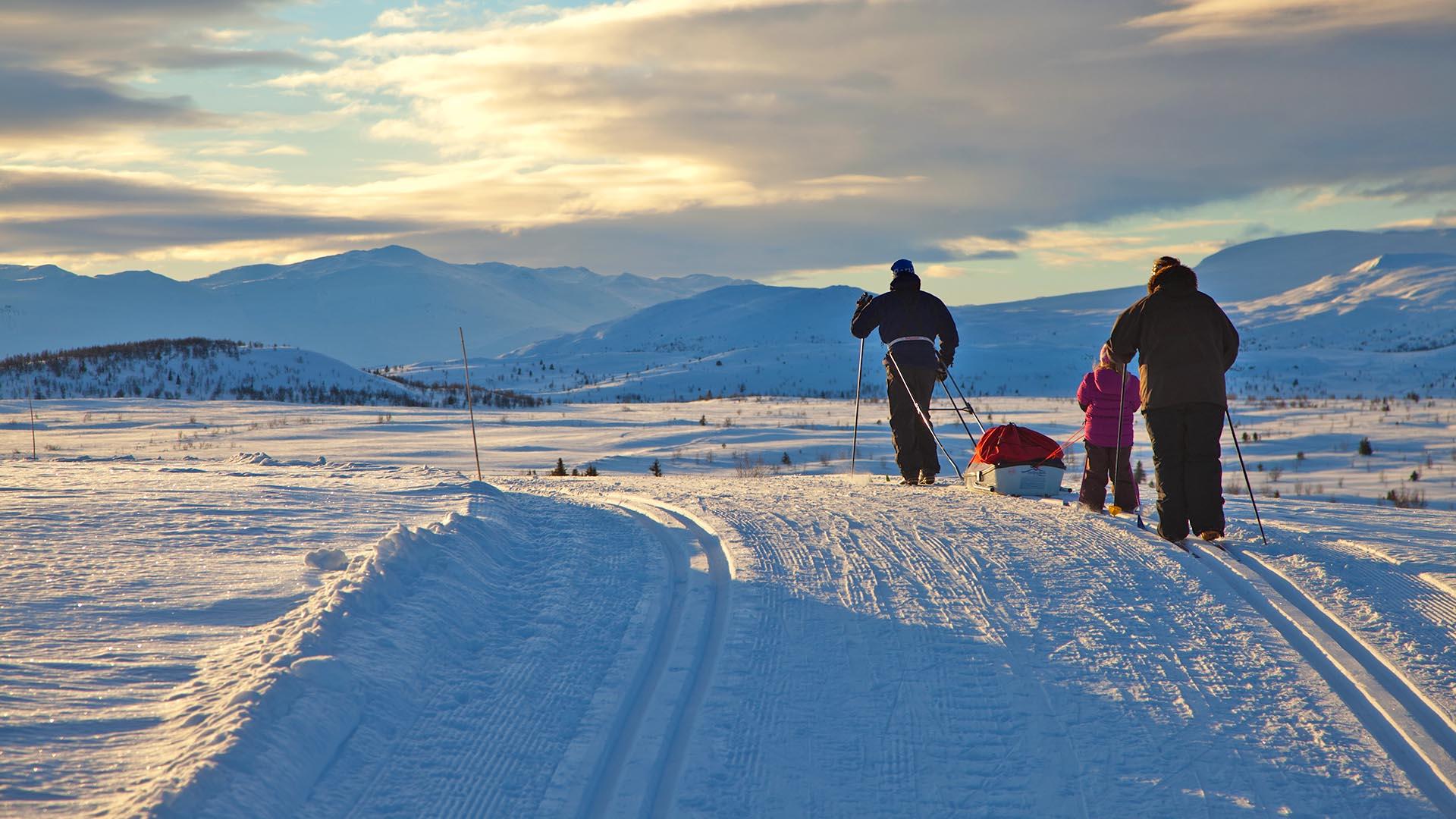 Familie på skitur med pulk i Vasetområdet, fjell i bakgrunnen.