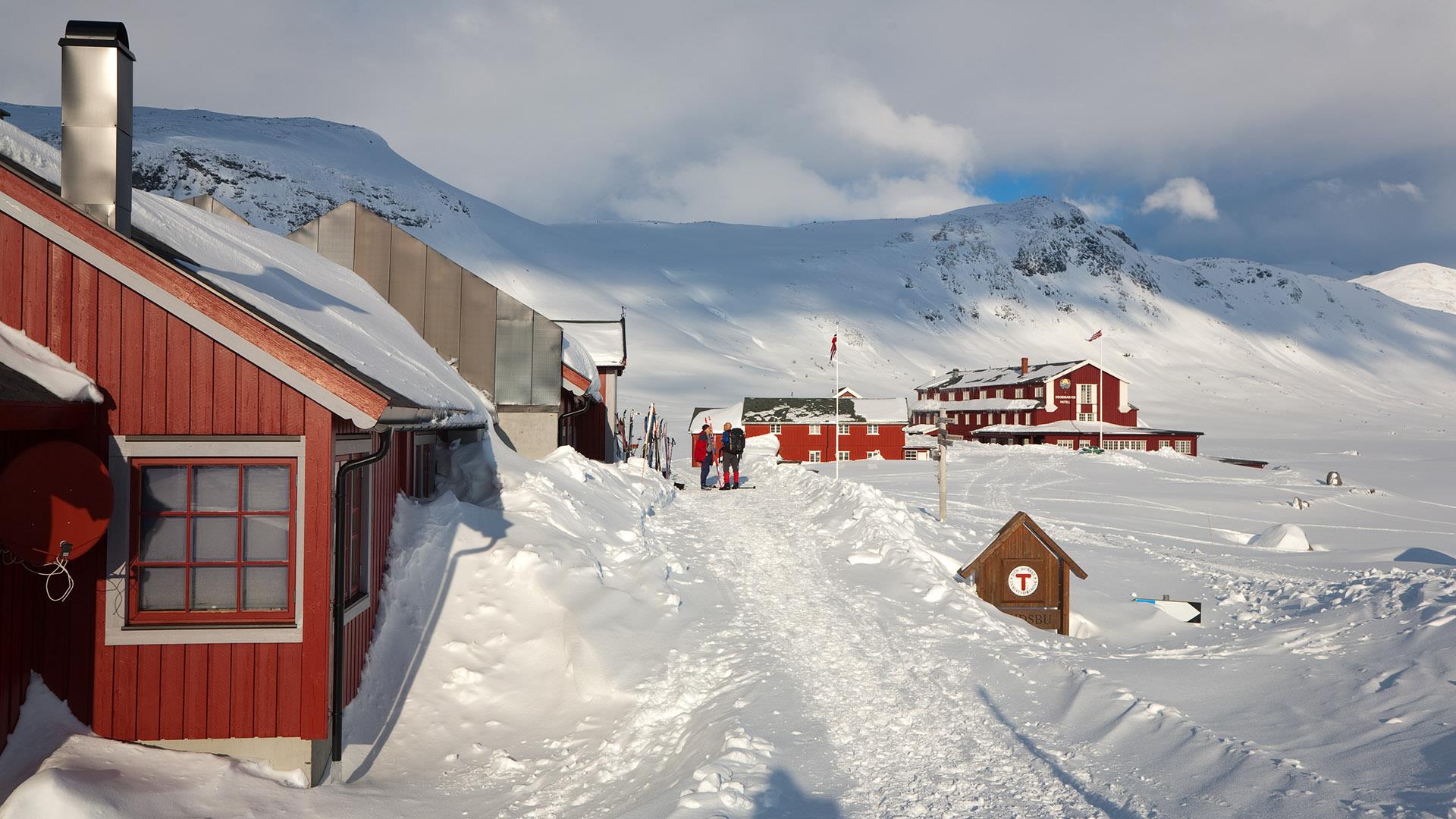 Red wooden buildings (one tourist cabin and one hotel) in the mountain at wintertime with lots of snow