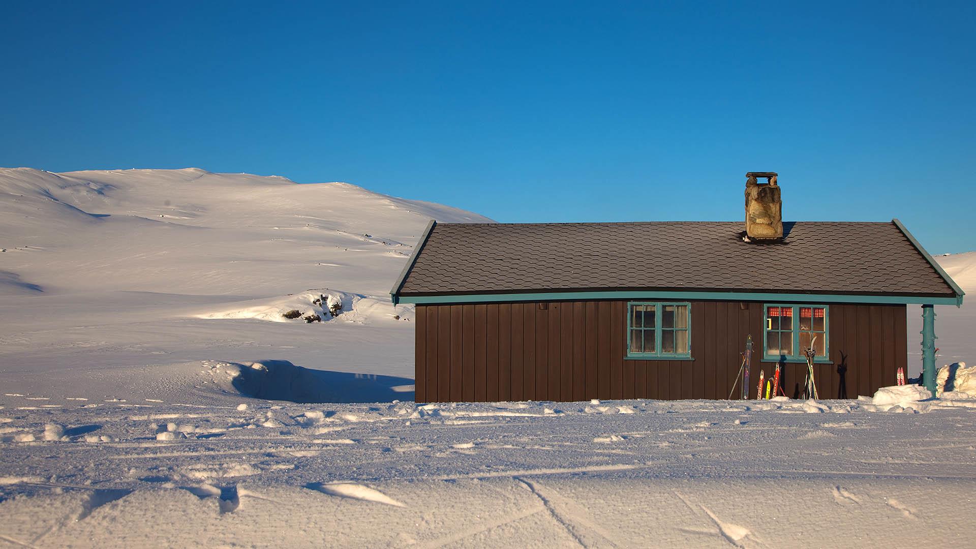 Eine Berghütte in schneebedeckter Fjellandschaft mit blauem Himmel