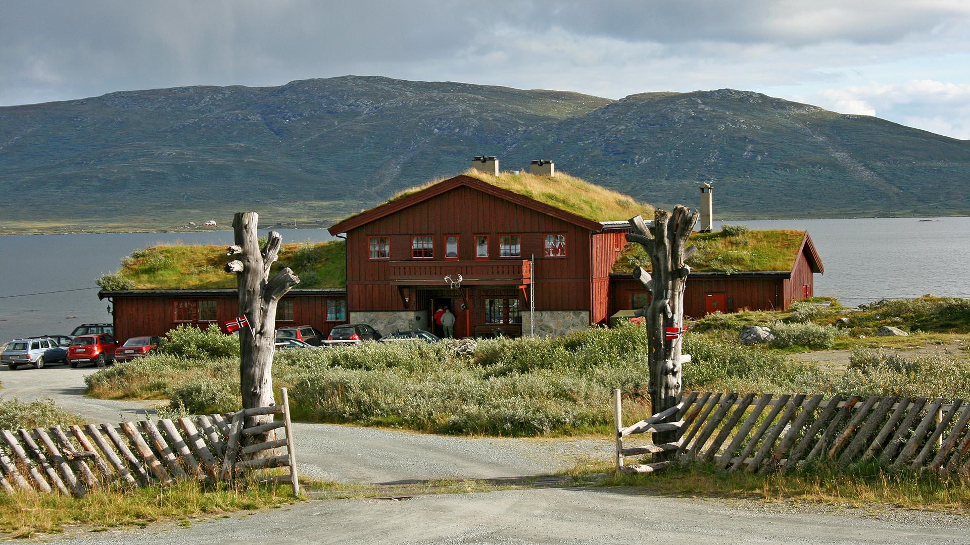 En fjellstue med gresstak ved et vann i fjellandskap