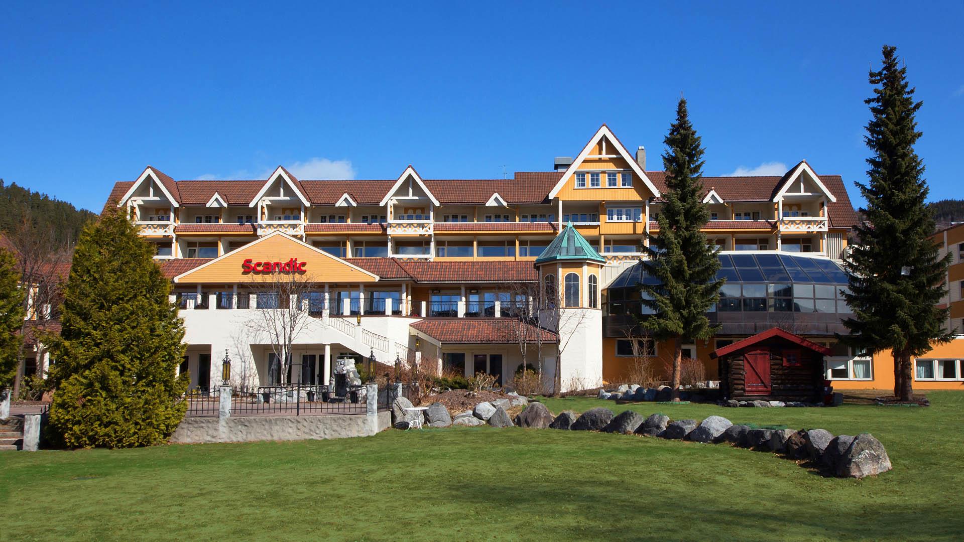 Yellow wooden hotel in swiss style seen from the garden side with lawn and coniferous trees and bushes
