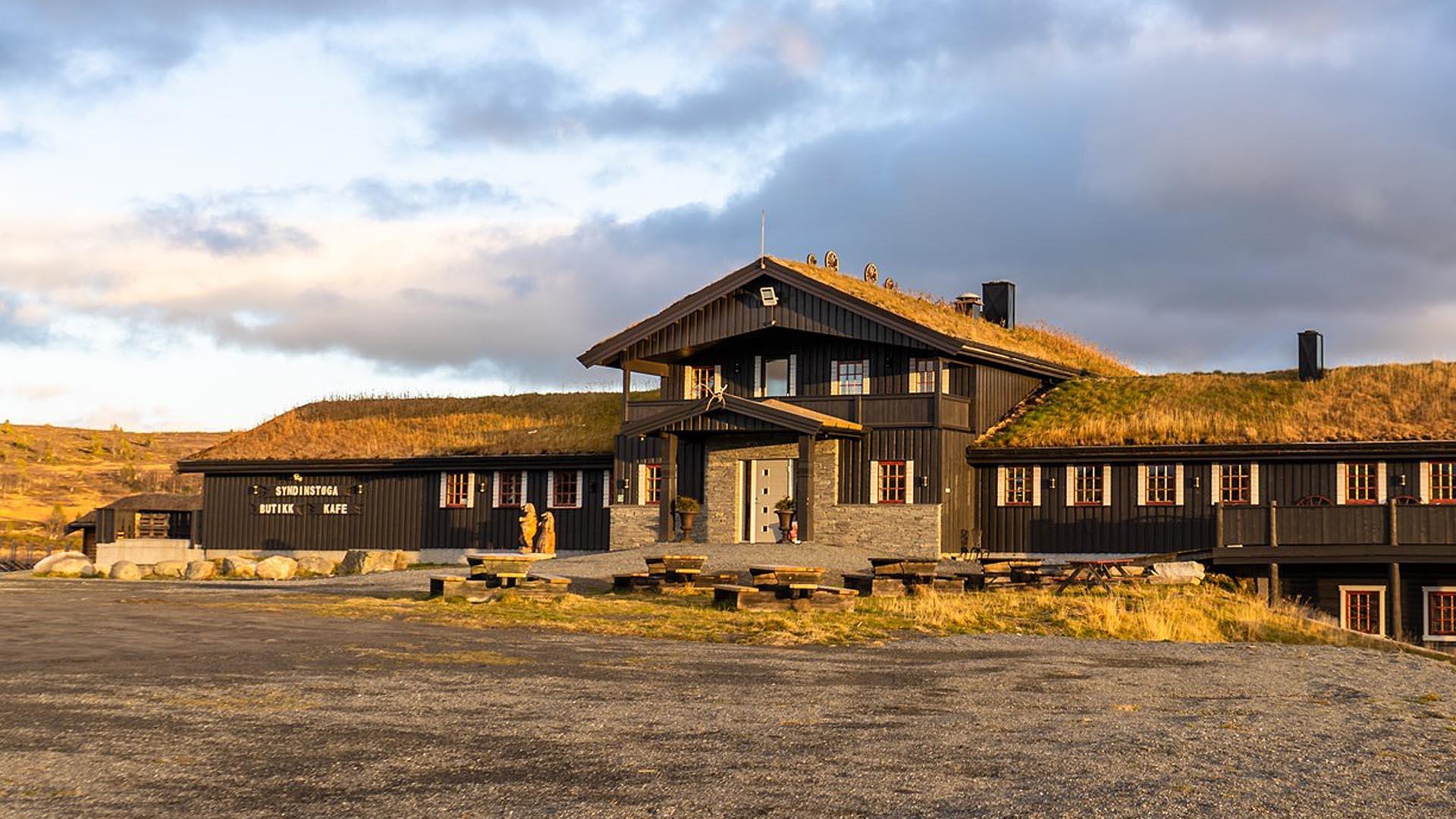 A mountain lodge with wood and stone panel and grass roof in evening sunlight