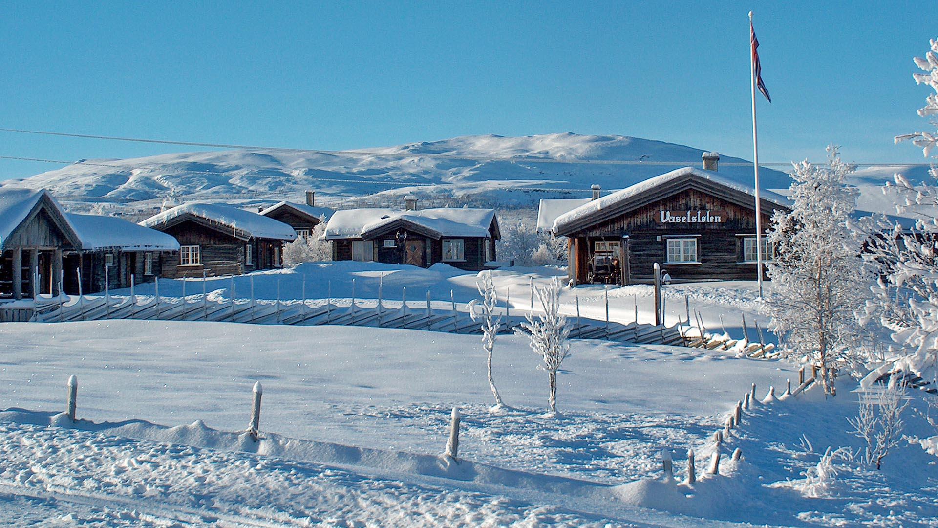 Hütten in weißer Winterlandschaft im Fjell. Blauer Himmel, norwegische Flagge