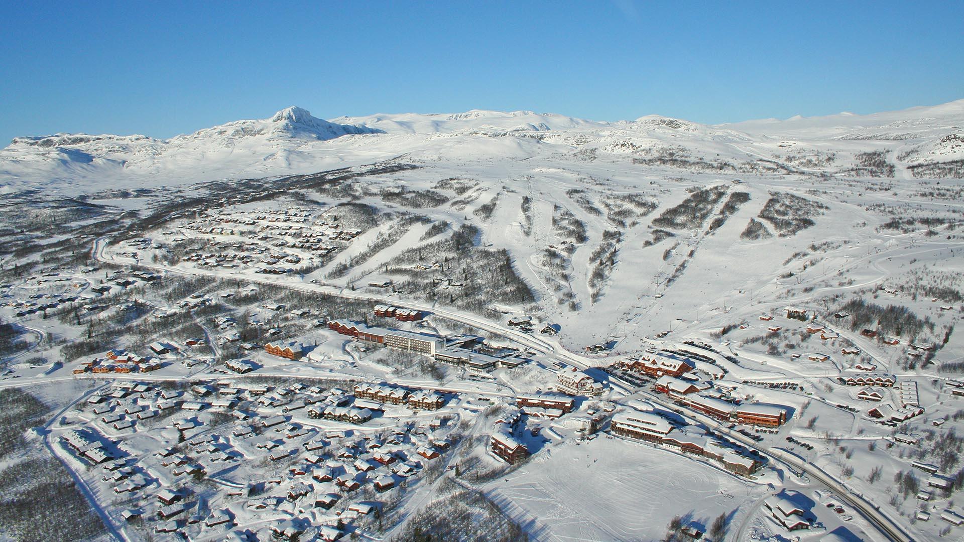Vinter-luftfoto som viser en fjellandsby med alpinanlegg og fjell i horisonten