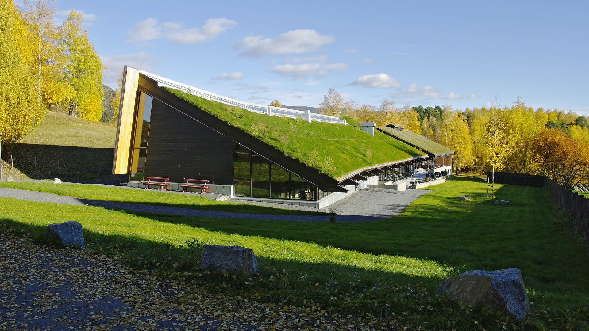 A modern triangular building with an asymetrical roof where there's grass on the less steep side.