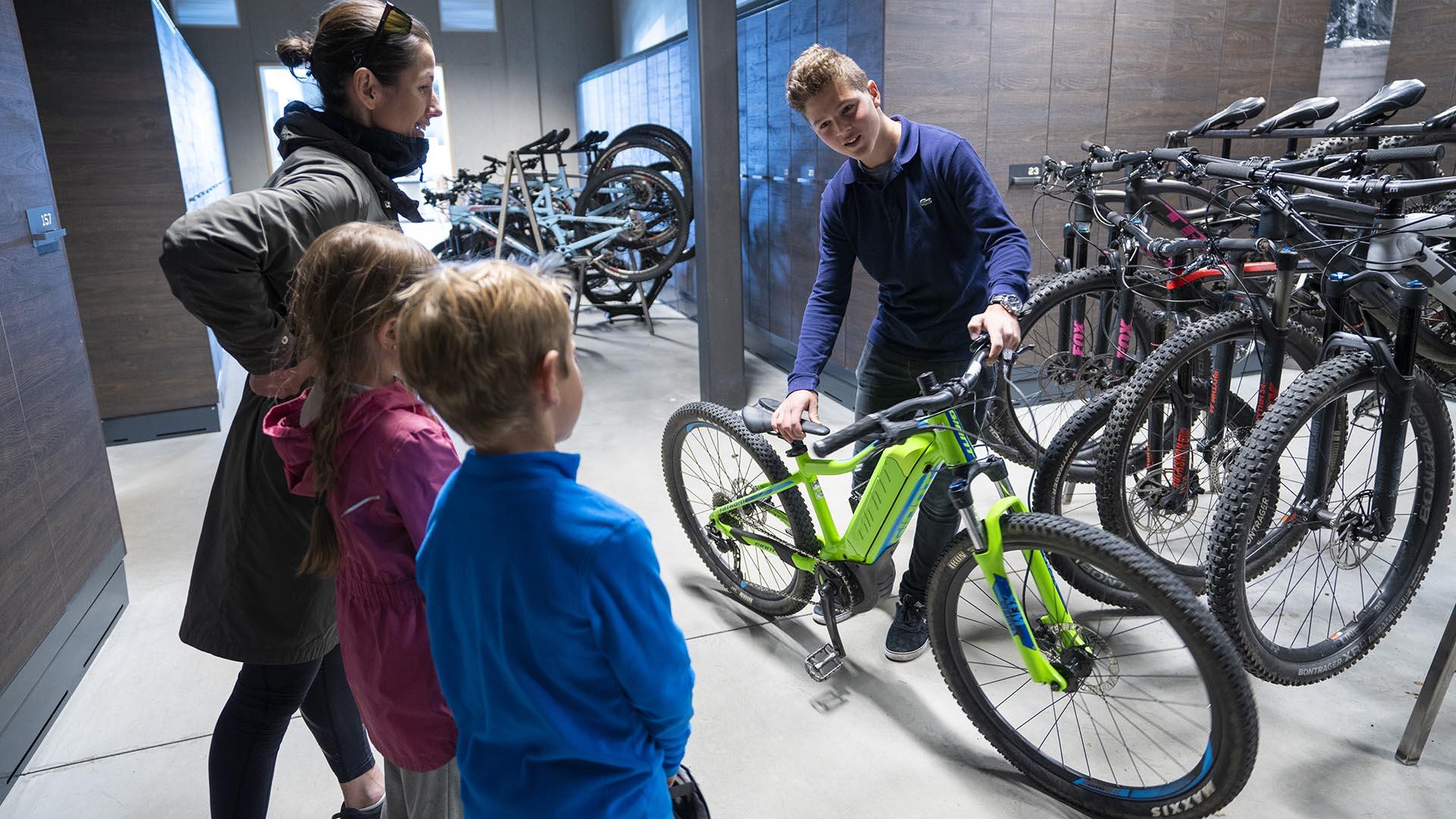 A staff member in a bicycle rental shows a mountain bike to a family.