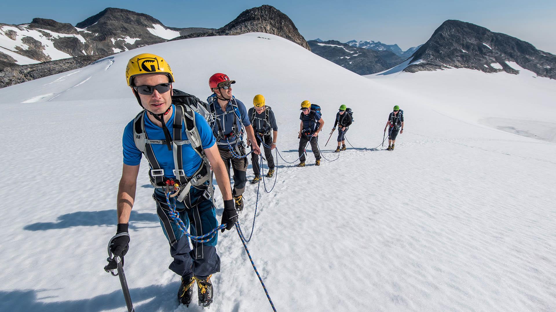 A roped-up group of hikers on a glacier which is surrouded by mountains