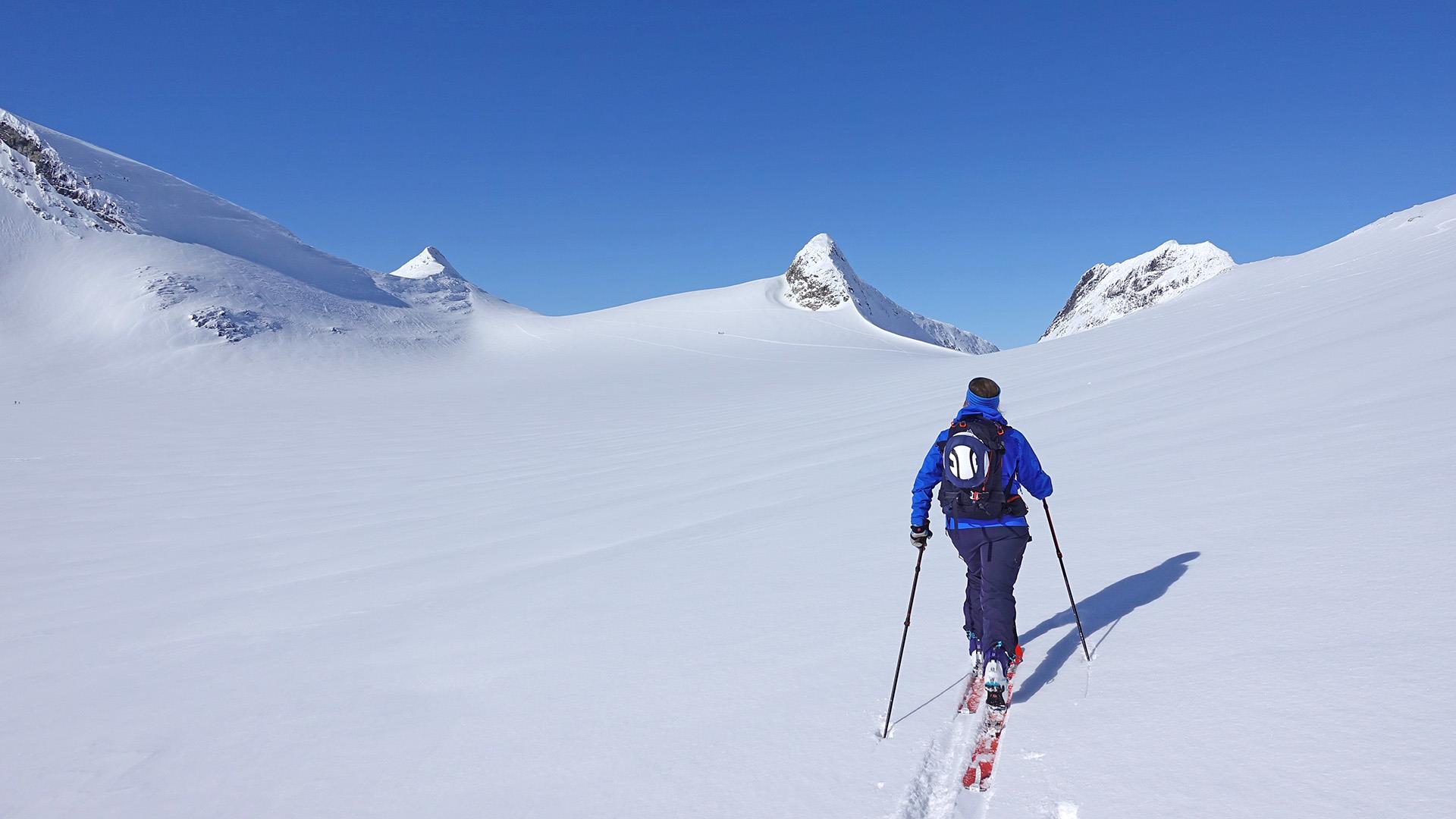 Ensom randonekjører på tur oppover fjellene i jotunheimen på vinteren.