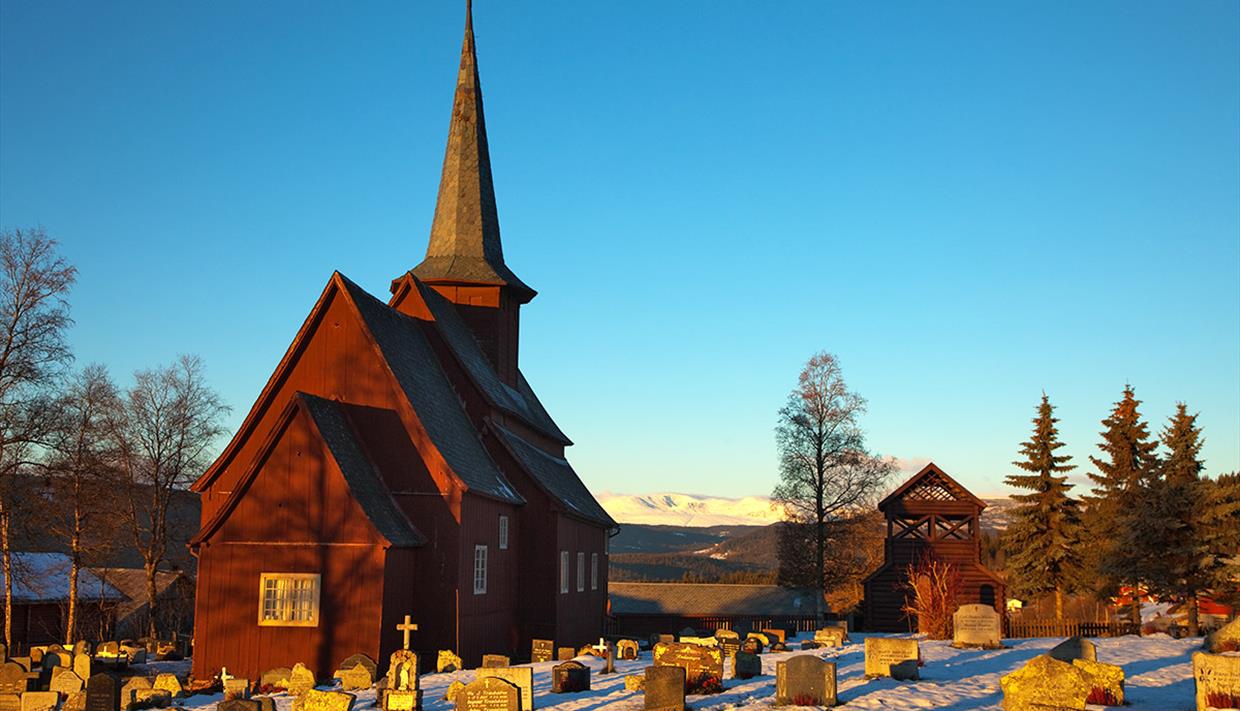 En stavkirke i en snødekt kirkegård i vintersolskinn.