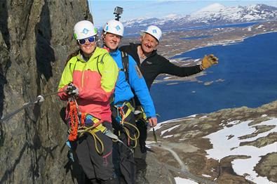 Tre klatrere i bratt fjellside med utsikt mot vann og fjell