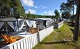 Permanent caravans with wooden deck and outdoor furniture, white fence and green lawn.