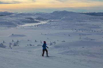 Skiløper med fantastisk skue over fjell-landskap i solnedgang.