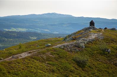 The last few steps towards the summit cairn at Jutulen with forested hillsides and a higher mountain in the background.