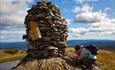 A large summit cairn on Synet. A mother and a child register their trip in the tour log book.