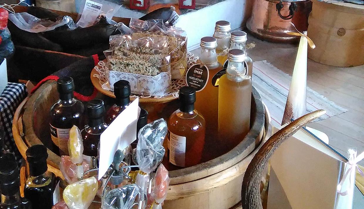A wooden bowl filled with delicious local produce: herb oils, berry syrup, cellophane bags with baked goods and sweets.