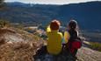 To barn sitter på en fjellpynt med utsikt ned i en dal