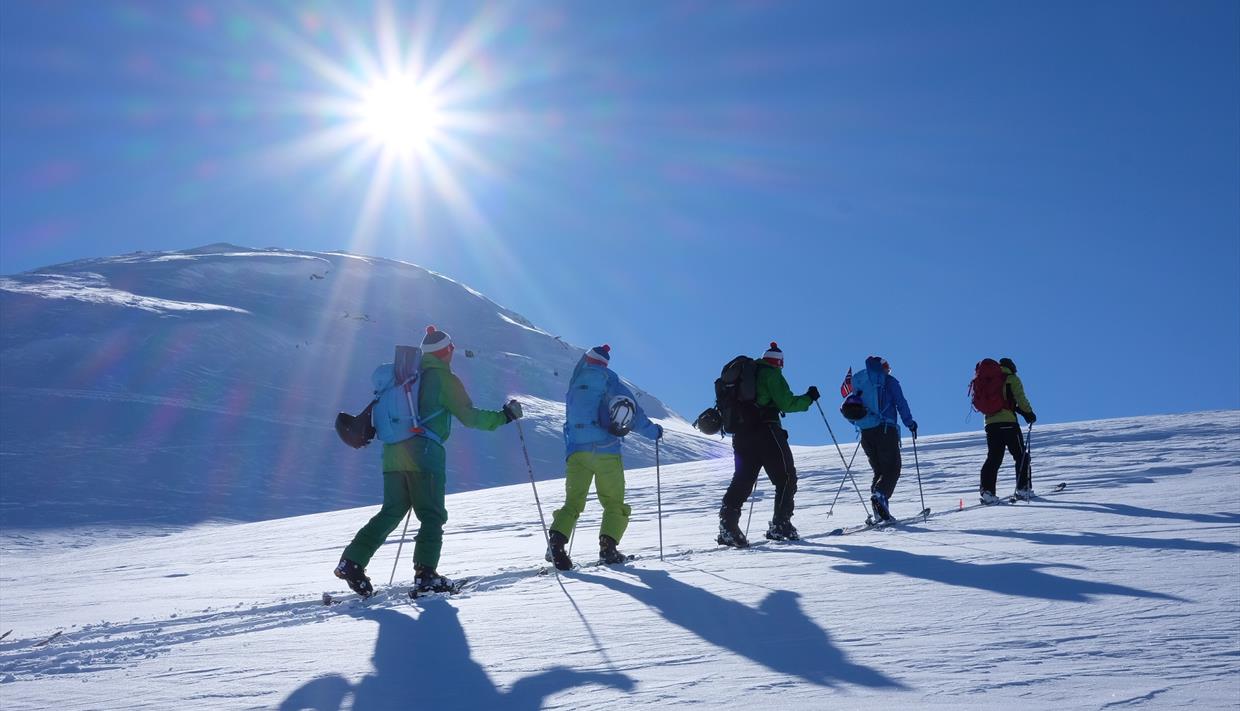 En gruppe går oppover fjellet i strålende solskinn og fantastiske snøforhold.