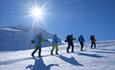 En gruppe går oppover fjellet i strålende solskinn og fantastiske snøforhold.