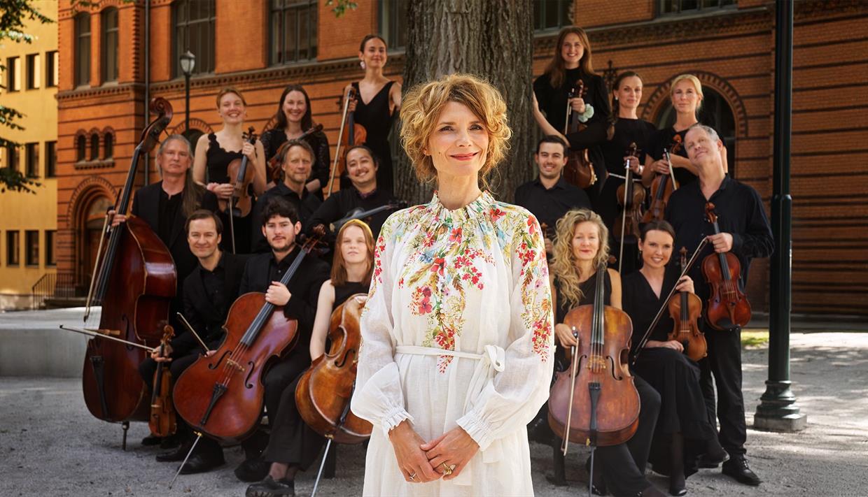 Bilde av Herborg med orkesteret i bakgrunn. Bilde av Herborg med orkesteret i bakgrunn.