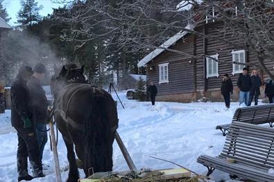 A horse with a sleigh on a farm yard in the snow with persons standing around.