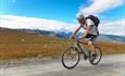 Syklist på vei opp bakkene på Slettefjellveien med Jotunheimens tinder i bakgrunnen.